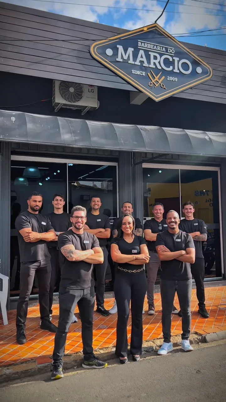 Equipe da Barbearia do Márcio diante da fachada, com o letreiro dourado acima