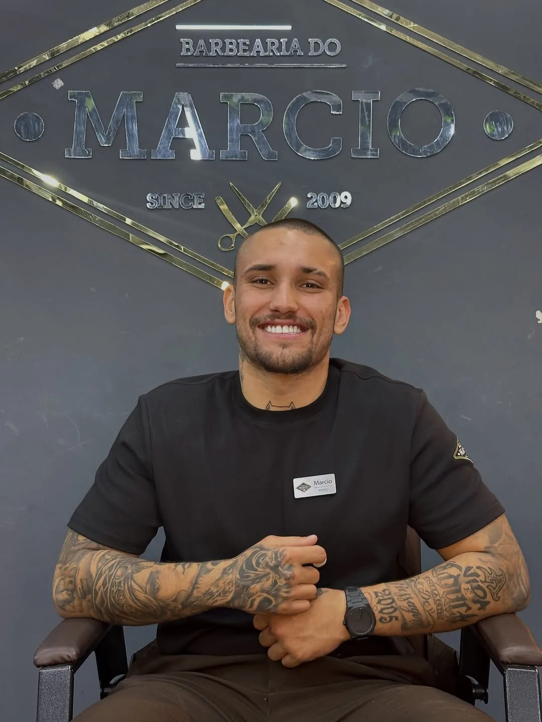 Barbeiro sentado sob o letreiro da Barbearia do Márcio